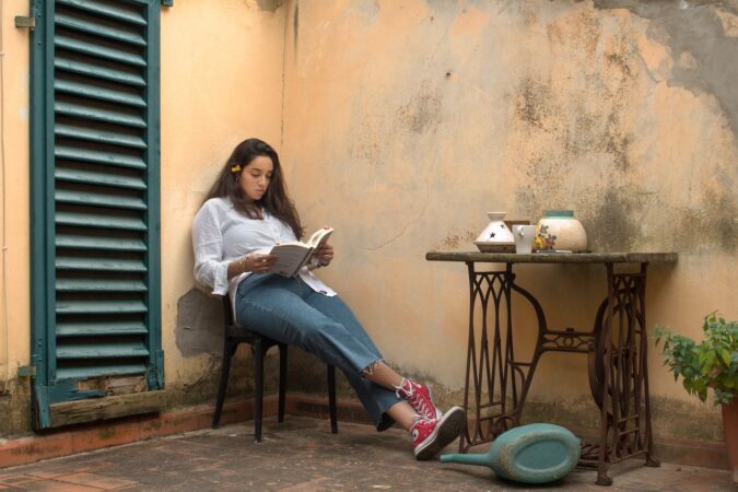 Kobieta czyta książkę siedząc na krześle przed domem